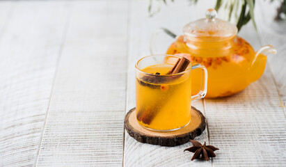 Autumn sea buckthorn tea in a mug with a cinnamon stick and in a teapot on a white wooden background. Autumn mood.