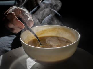 a hot bowl of soup with a hand and a spoon