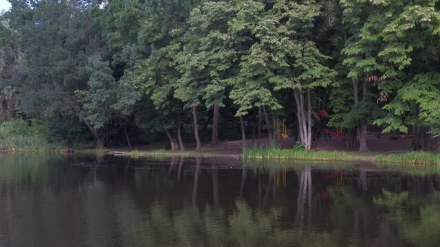 Pond with green water among lawns and trees against buildings of city.