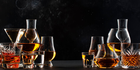 Strong alcoholic drinks, spirits and distillates iset in glasses: cognac, scotch, whiskey and other. Black bar counter background
