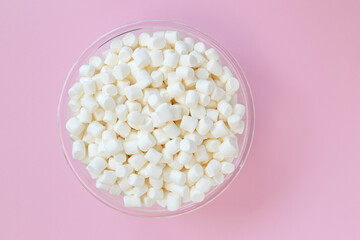 white marshmallows in bowl on pink background, top view