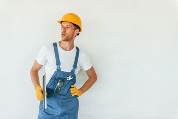 Standing near white wall. Young man working in uniform at construction at daytime