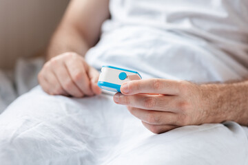 Health care. Close up of hands of hospitalized patient, lying at bed and holding a pulse oximeter. Concept of determination of oxygen in the blood