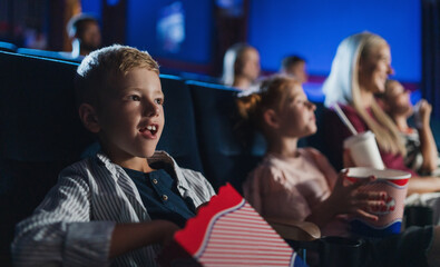 Small boy with family sitting and watching film in the cinema, eating popcorn.