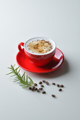 Latte coffee in red mug decorated with caramel and chocolate motifs. Coffee beans are part of the composition.
