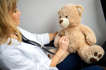 Friendly young doctor female pediatrician examining plush teddy bear with help of stethoscope