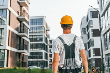 Rear view. Young man working in uniform at construction at daytime