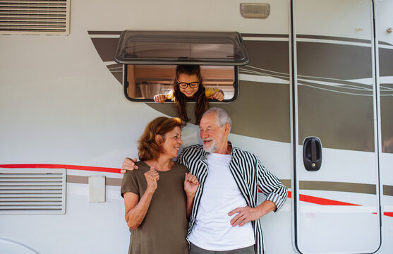 Senior Couple With Granddaughter Standing By Car, Caravan Family Holiday Trip.