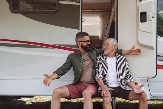 Mature man with senior father sitting by car outdoors, fun on caravan holiday trip.