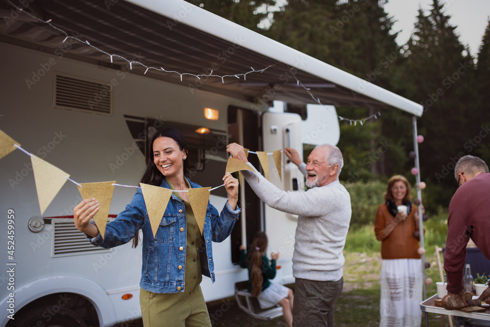 Wall mural Multi-generation family preparing party by car outdoors in campsite, caravan holiday trip.