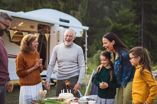 Multi-generation family celebrating birthday outdoors at campsite, caravan holiday trip.