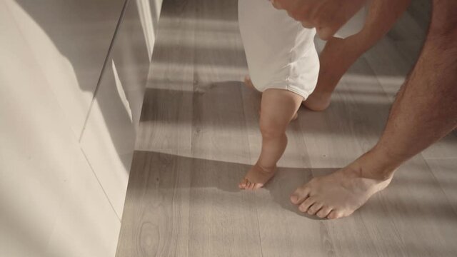 Baby taking first steps. The father holds and supports the child and teaches him to walk at home. First year of a child's life. High quality 4k footage