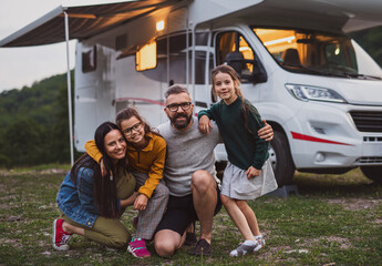 Happy family looking at camera outdoors at dusk, caravan holiday trip.