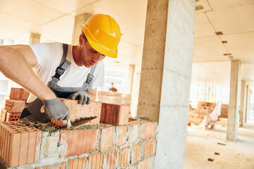 Working by using bricks. Young man in uniform at construction at daytime