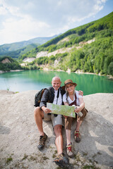 Happy senior couple on hiking trip on summer holiday, using map.