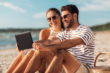 Fototapeta premium leisure and people concept - happy couple with tablet pc computer and picnic basket on summer beach
