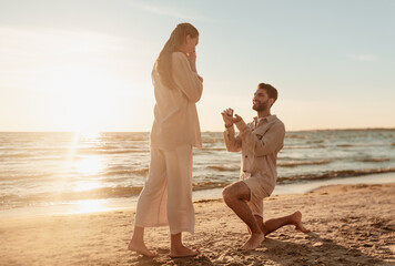 love and people concept - smiling young man with engagement ring making proposal to happy woman on...
