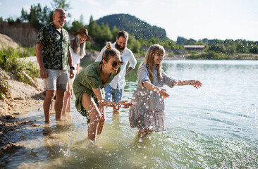 Happy multigeneration family on walk by lake on summer holiday, having fun in water.
