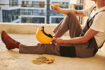 Sitting on the floor. Young man working in uniform at construction at daytime