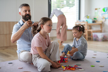 Father with three daughters indoors at home, playing and making hair.