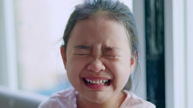 A young Asian girl is crying with tears in her eyes, her mouth wide open and her teeth are white.