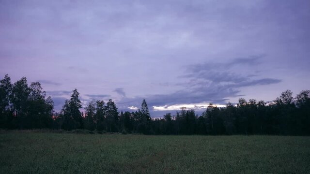 Timelapse of sunrise with crazy colours over a meadow with a forest in the background