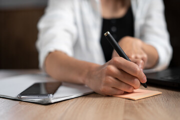 Business lady taking notes while working in the office. Woman's hand with a pen close-up. The manager is writing something handwritten at the table. Business and work.