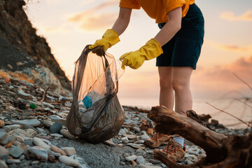 Earth Day. Close up of volunteer's hands in rubber gloves puts a dirty plastic bottle in bag. Sunset on the background. The concept of ecology disaster