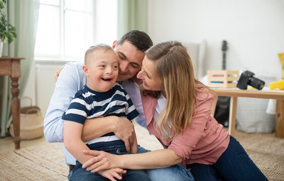 Cheerful down syndrome boy with parents indoors at home hugging, laughing.