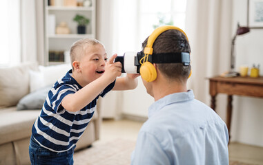 Father with happy down syndrome son indoors at home, using vr goggles.
