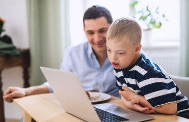 Father with happy down syndrome son indoors at home, using laptop.