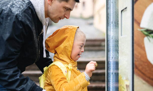 Happy down syndrome boy with father outdoors on a walk in rain, playing.