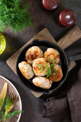 Turkey cutlets in a black frying pan on a brown cooking table top view