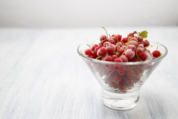 Frozen red currants in a glass vase on a white wooden table. Close-up.