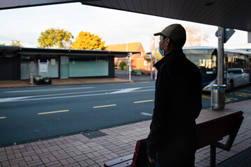 Man wearing a face mask waiting at bus stop shelter with an approaching bus