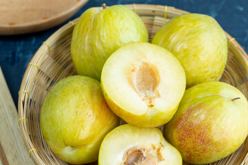 Top view Rotate Fresh Green plum or Flavor Grenade Pluot closeup, Green plum in Bamboo basket on wooden table in garden.