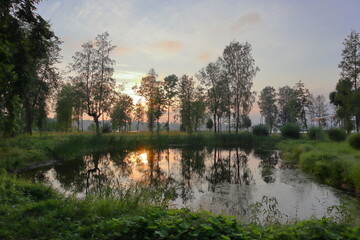 reflections of trees and the sky in the reservoir of the park, surrounded by greenery and trees, at a colorful sunset