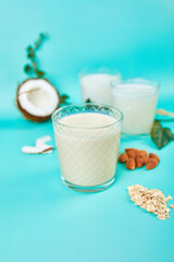 Various vegan plant based milk and ingredients, non-dairy milk, alternative types of vegan milks in glasses on a blue background with copy space