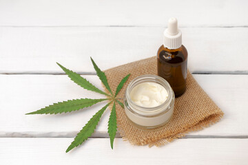 CBD-Infused Face cream and serum with cannabis green leaf on white wooden background with copy space