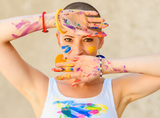 Playful portrait of a young gorgeous female painter artist, with hands covered in paint, looking...