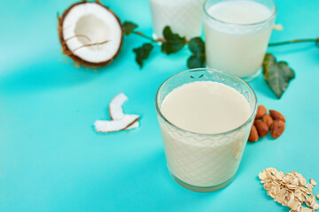 Various vegan plant based milk and ingredients, non-dairy milk, alternative types of vegan milks in glasses on a blue background with copy space