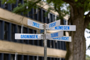 Closeup of direction sign in front of school building pointing at several Dutch cities such as Zwolle, Groningen, Nijmegen, Utrecht, Tilburg, Maastricht