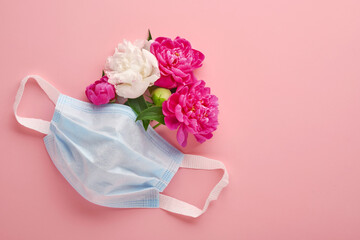 Protective medical face mask with peonies flowers on pastel pink background. Disposable surgical mask as symbol of coronavirus or covid-19 pandemic protection. Valentine, Women or Mother day concept.