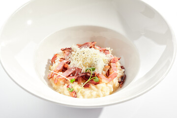 Risotto alla carbonara on white restaurant plate. Risotto with bacon and egg, garnished with micro greens. Risotto topped with parmesan cheese.