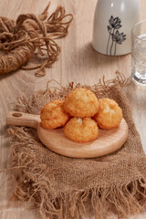 Toasted coconut cake in cutting board, mineral water, flowerpot on wooden table.  Soft Light. Nobody
