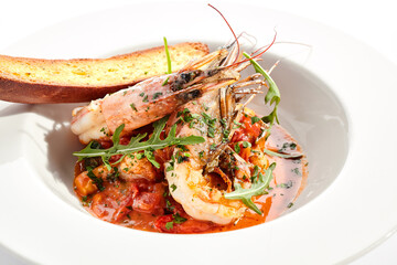 Seafood with tomato sauce on white restaurant plate. Shrimp seafood and tomato stew garnished with fried bread. Isolated on white background.