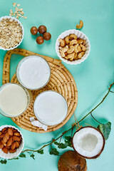 Various vegan plant based milk and ingredients, non-dairy milk, alternative types of vegan milks in glasses on a blue background , flat lay, top view with copy space