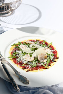 Beef carpaccio with mushrooms and parmesan cheese. Fancy dinning with beef carpaccio on white table with simple contemporary decor. Sunlight and harsh shadow still life. Beef carpaccio appetizer dish.