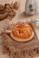 Croissant in cutting board, mineral water, flowerpot on wooden table. Soft Light. Nobody