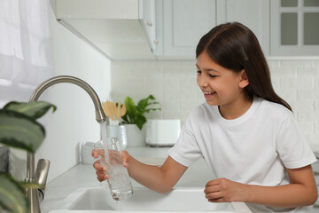 Girl filling glass with water from tap in kitchen